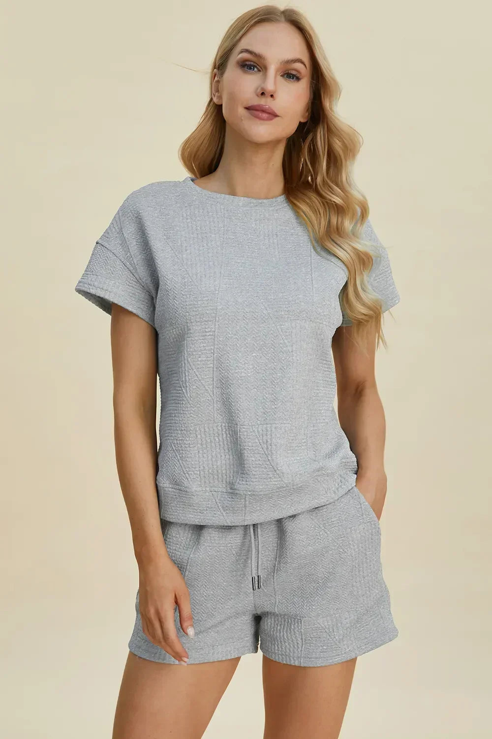 Woman wearing a light grey textured short-sleeve lounge set with matching drawstring shorts.