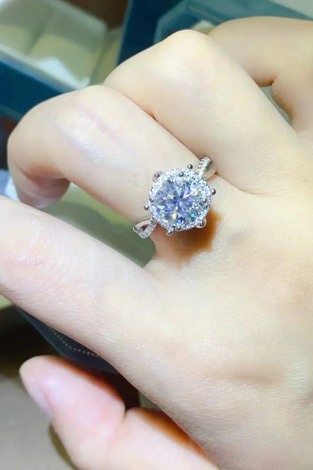 Hand wearing a sparkling diamond halo engagement ring with pavé band