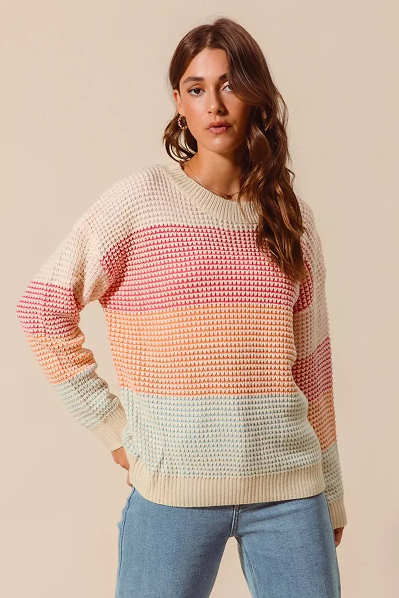 Woman wearing a relaxed fit pastel striped knit sweater and light blue jeans.