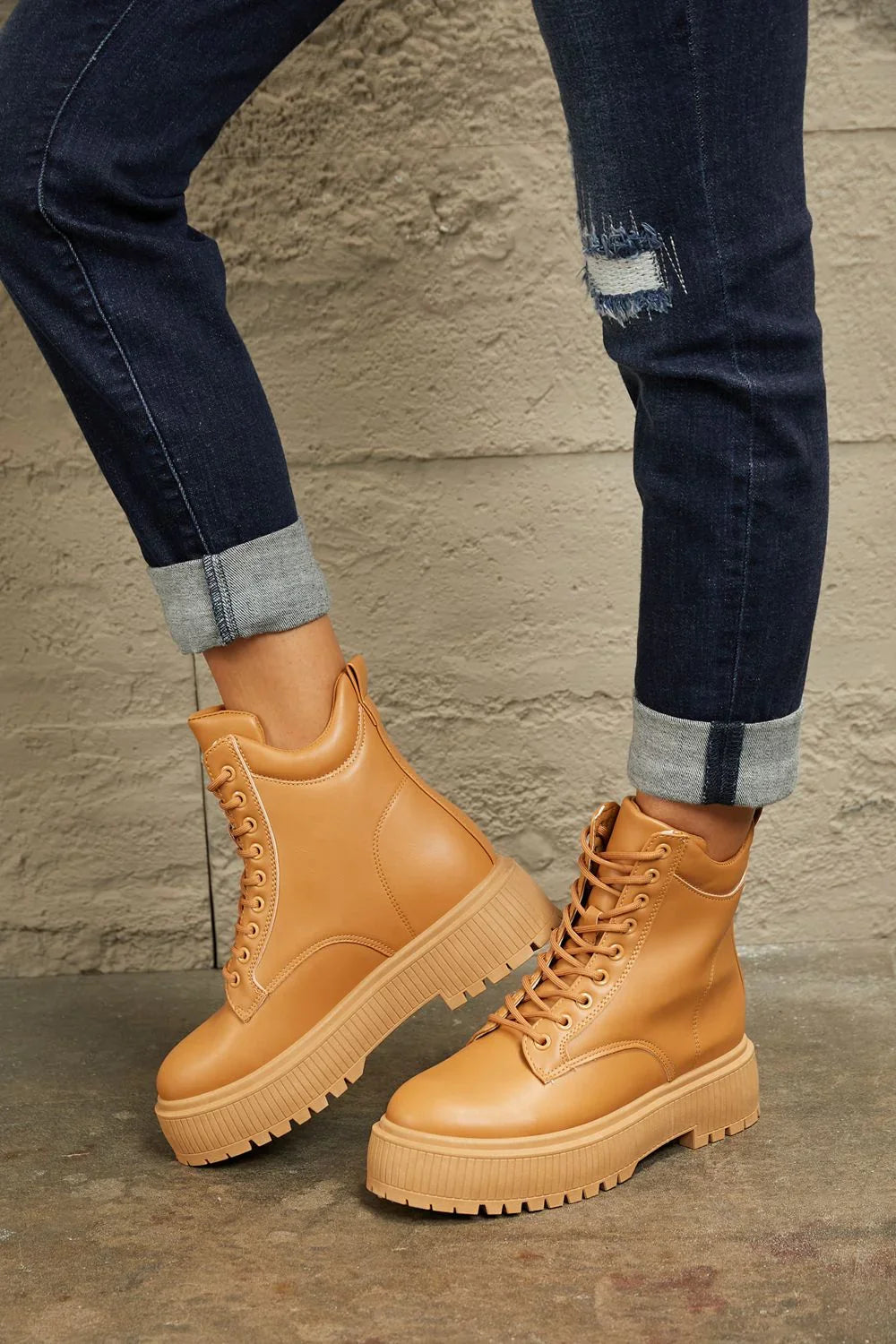 Tan platform lace-up boots styled with cuffed dark denim jeans on concrete