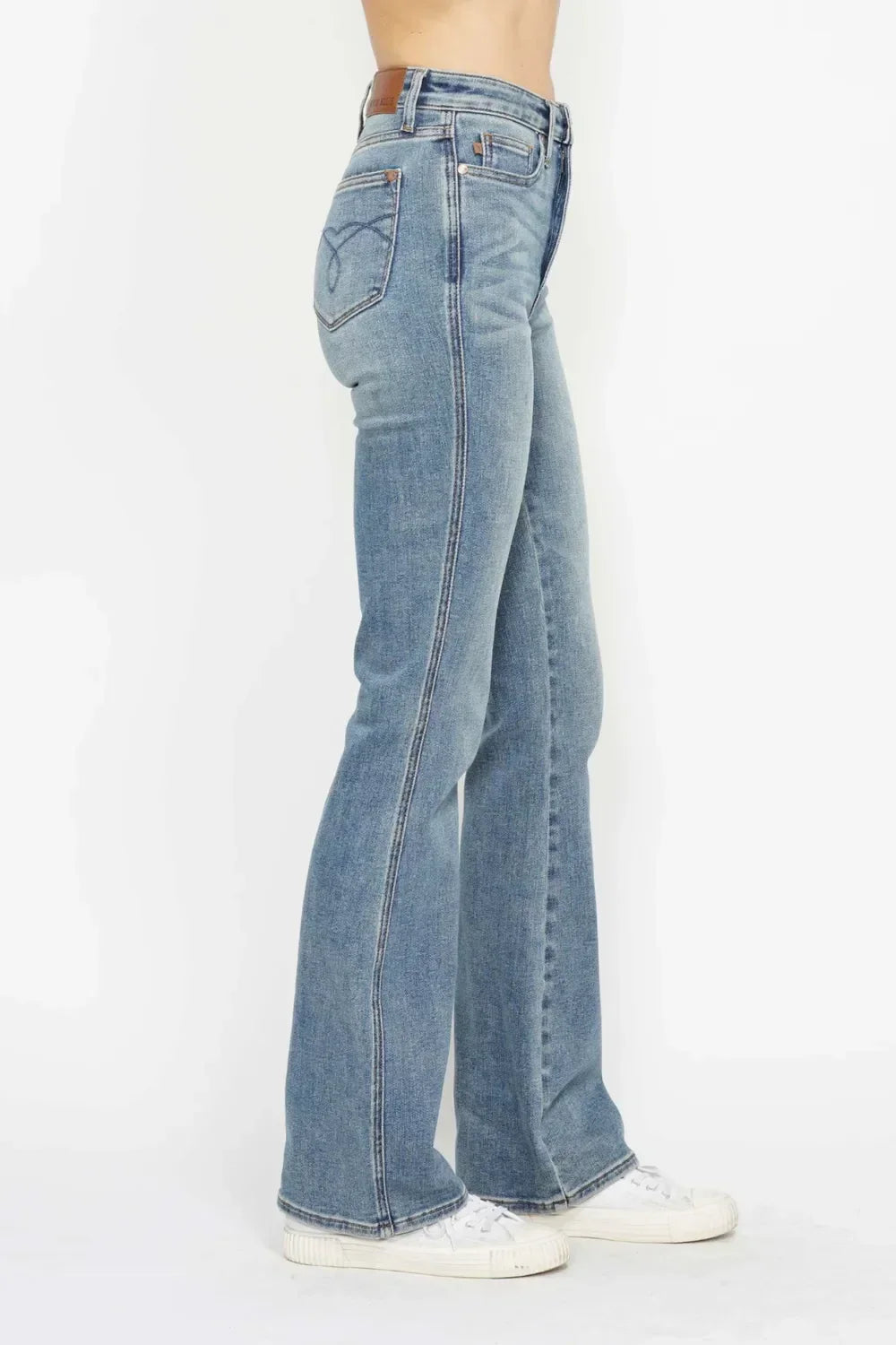 Woman wearing light blue high-waisted bootcut jeans and white sneakers on white background