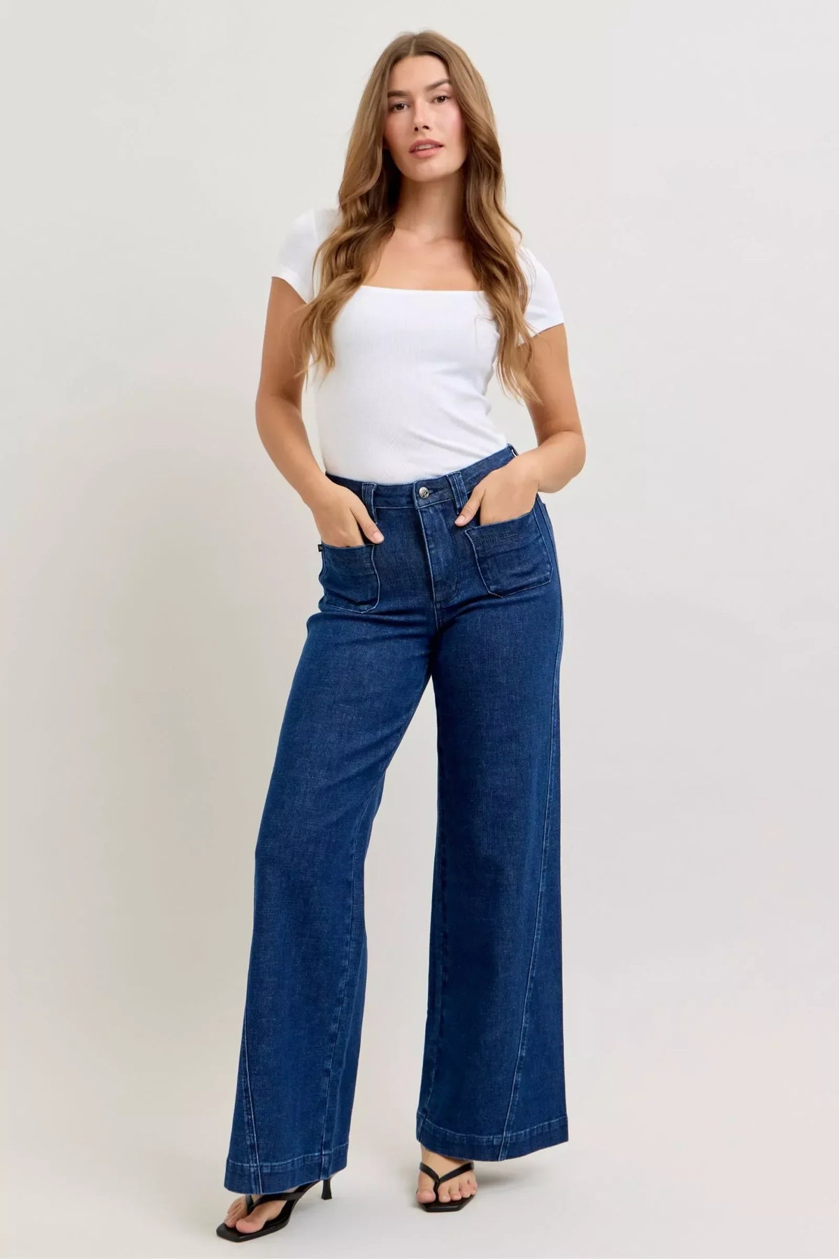 Woman in wide-leg high-waisted blue jeans and white square neck top, posing in studio
