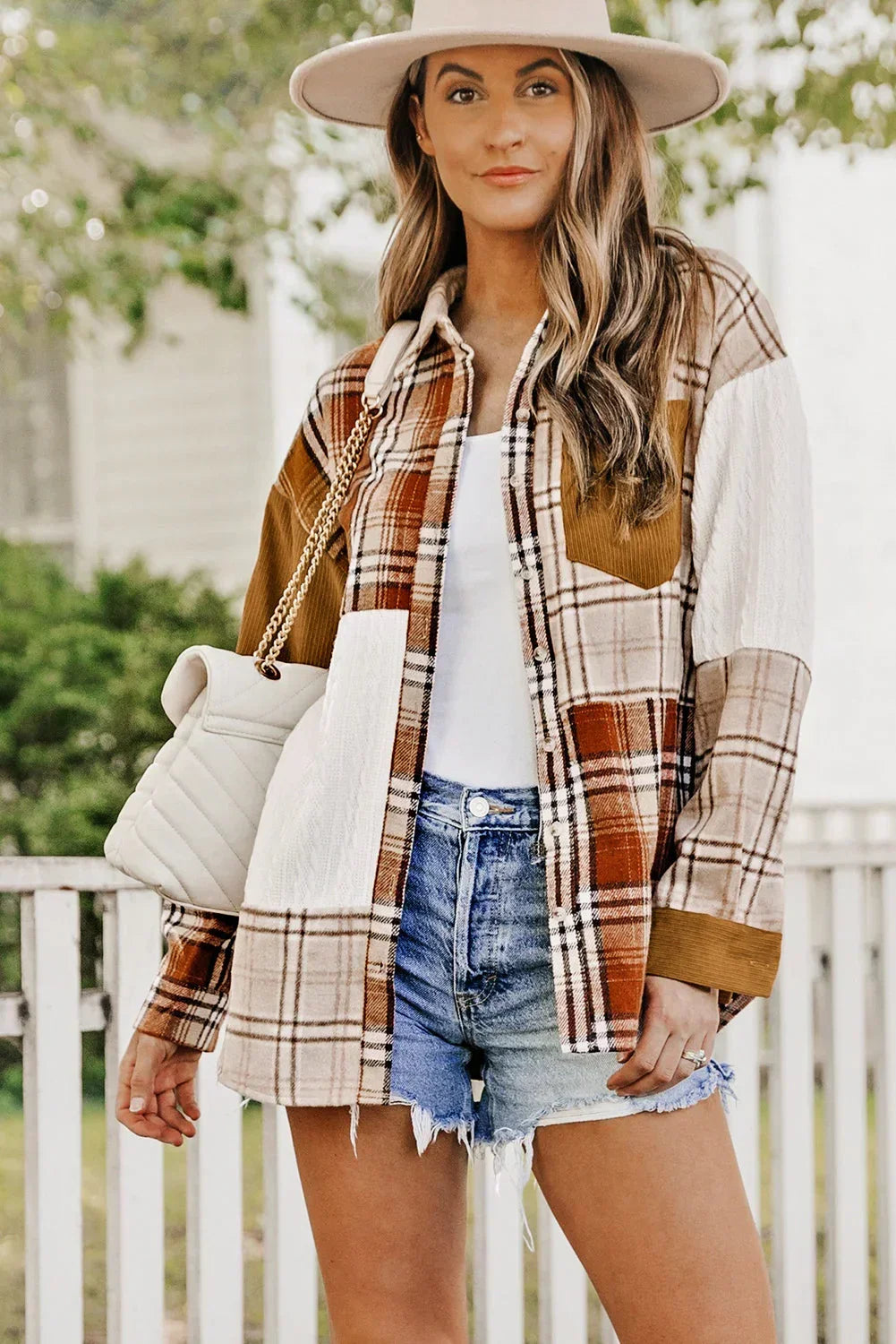 Woman in patchwork plaid shacket, denim shorts, white tank top, and wide-brim hat outdoors