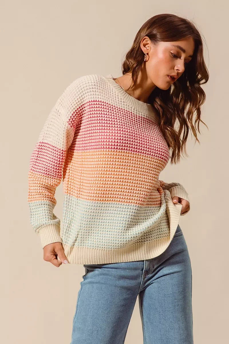 Woman wearing a pastel striped knit sweater with relaxed fit and light blue jeans