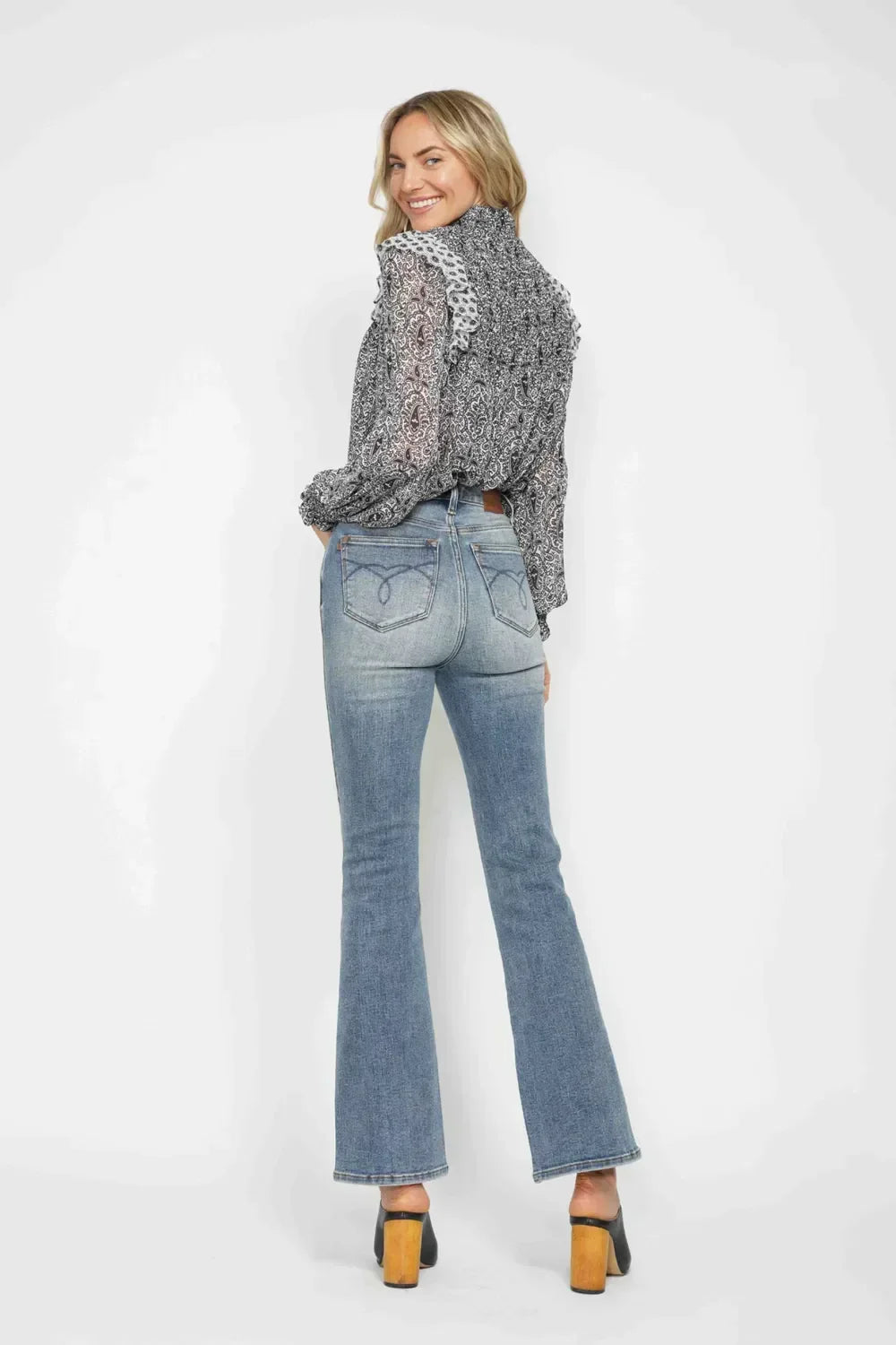 Woman wearing light wash flare jeans and a patterned long sleeve blouse, viewed from behind