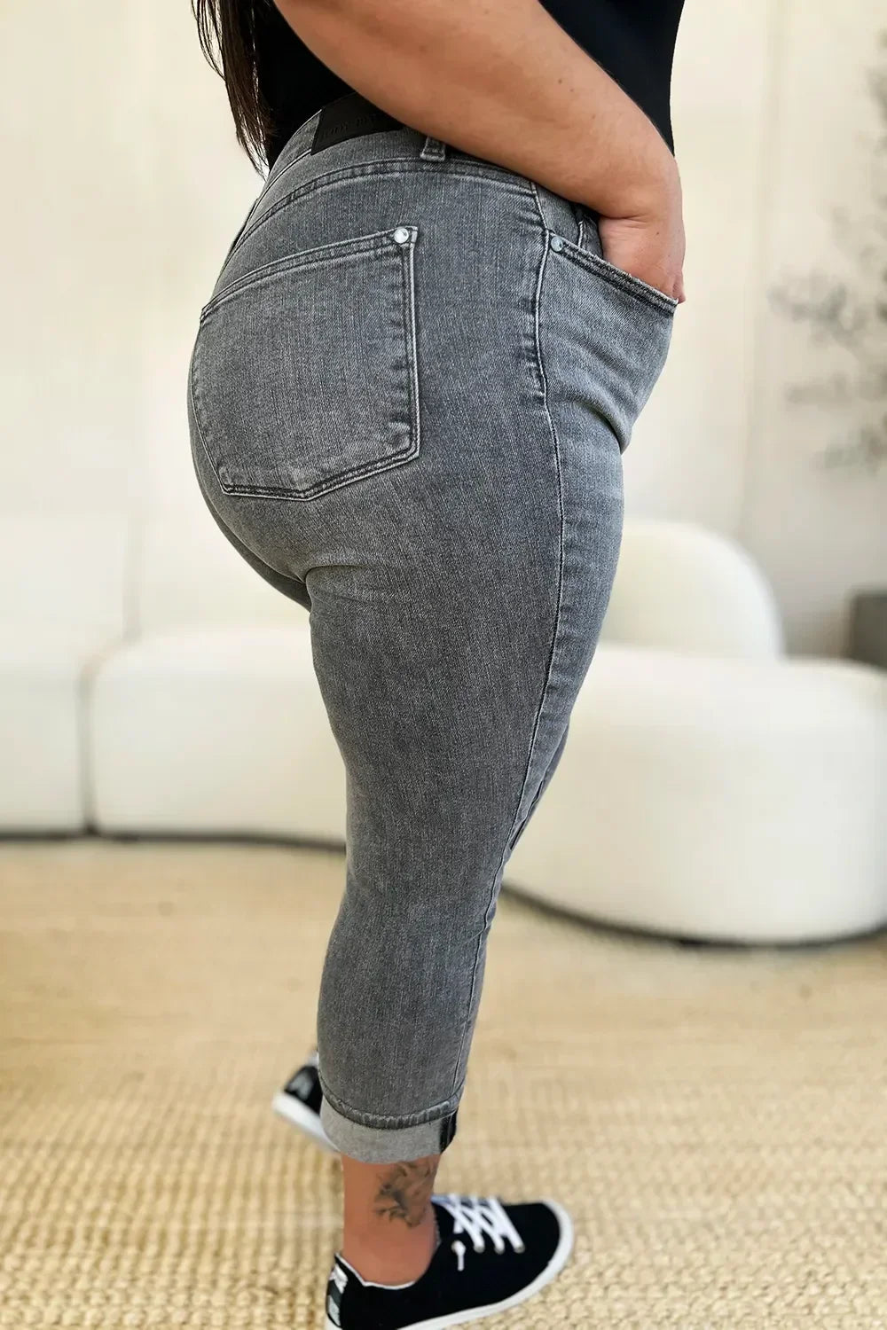 Side view of woman wearing grey cropped skinny jeans with rolled cuffs and black sneakers