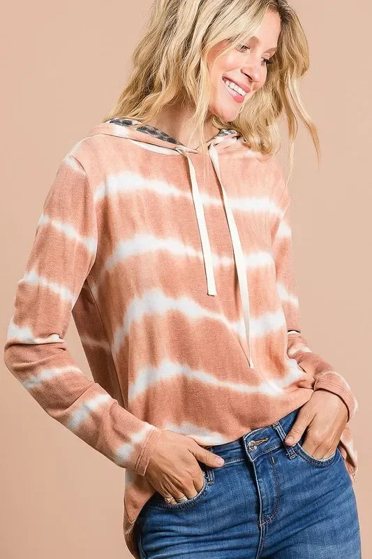 Woman wearing a relaxed fit, tie-dye hooded sweatshirt with drawstring and blue jeans.