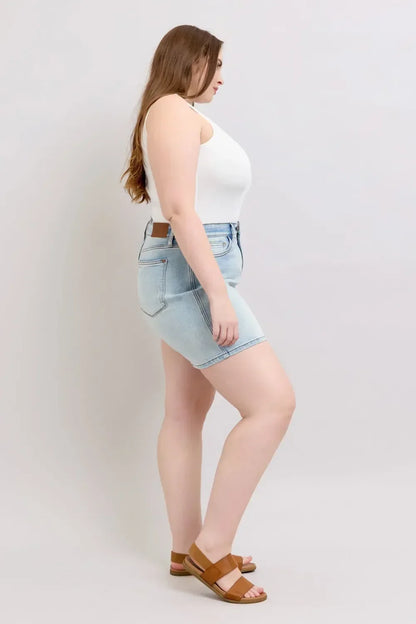 Woman in light wash denim shorts, white sleeveless top, and tan sandals, side view