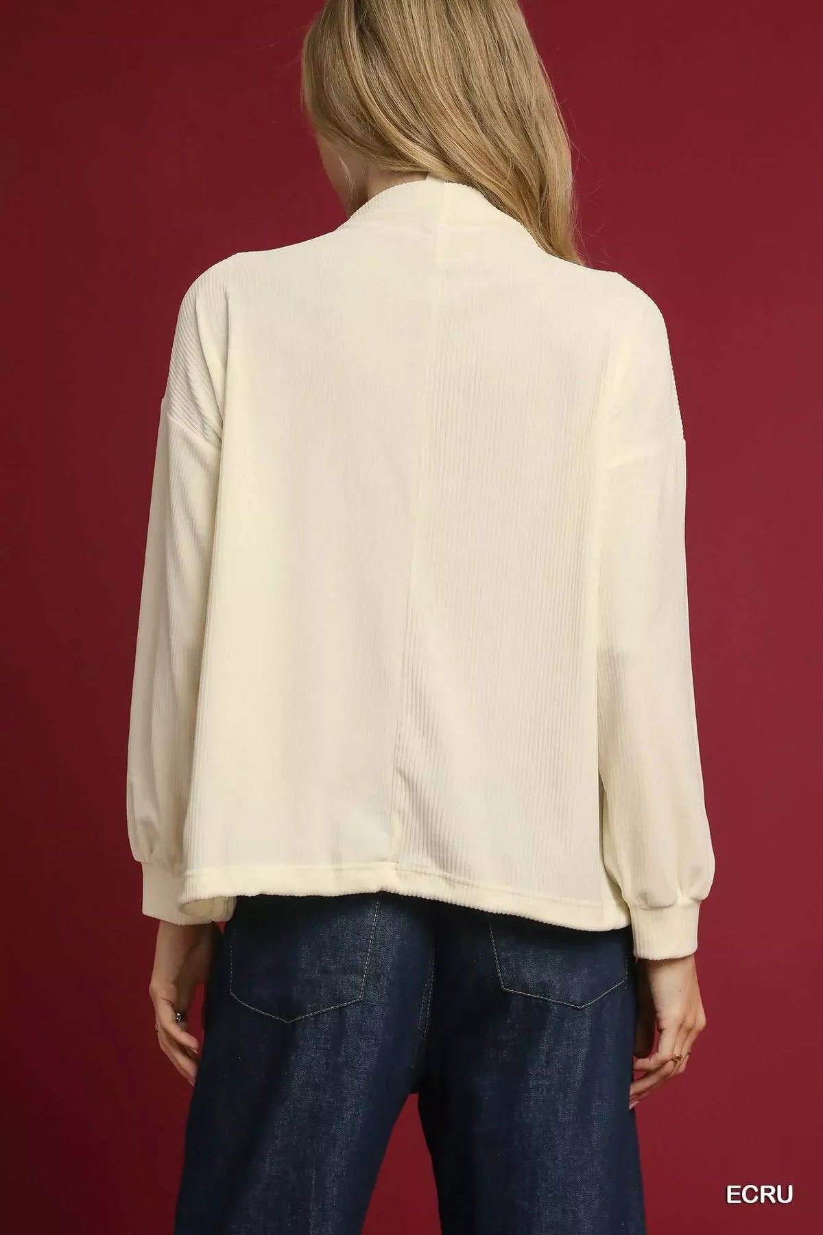 Back view of woman wearing an ecru long sleeve blouse and dark denim pants