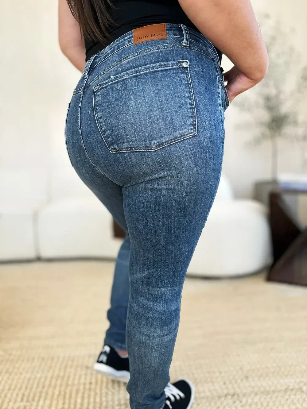 Back view of woman wearing high waist blue skinny jeans and black sneakers indoors
