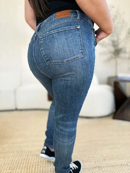 Back view of woman wearing high waist blue skinny jeans and black sneakers indoors