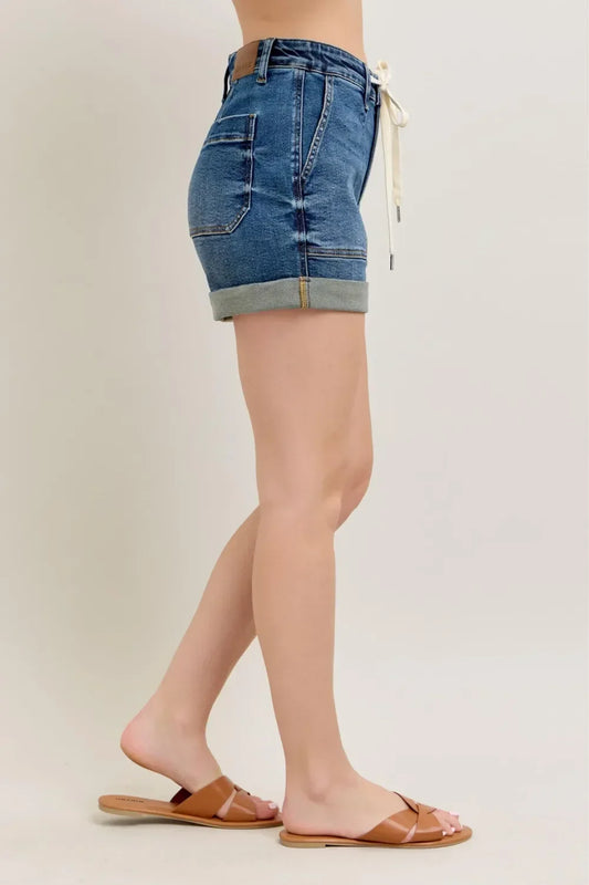 Woman wearing rolled hem denim shorts with side pockets and tan slide sandals