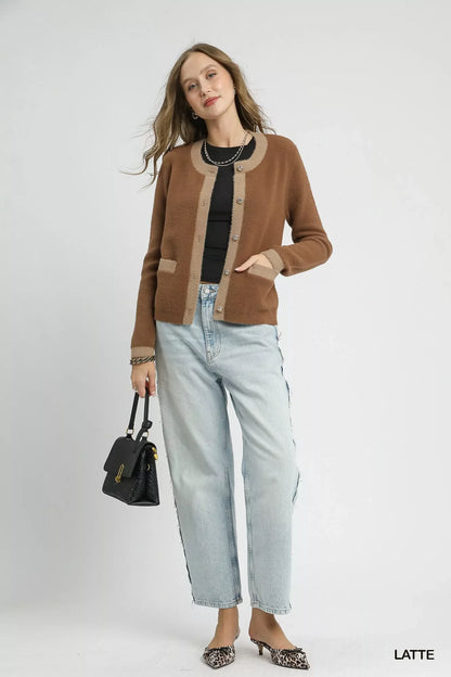 Woman wearing a brown cardigan with beige trim, black top, light wash jeans, holding black purse.