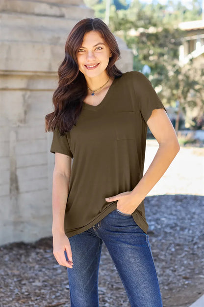 Woman wearing an olive green short sleeve V-neck top with front pocket and blue jeans outdoors.
