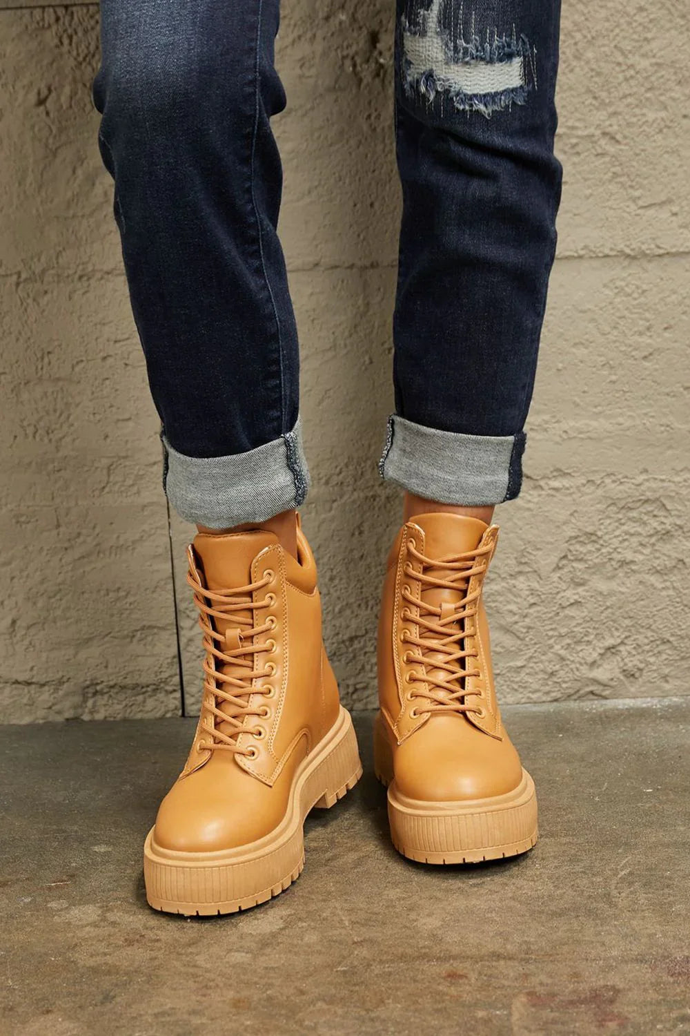 Tan leather lace-up combat boots paired with rolled dark-wash distressed jeans.
