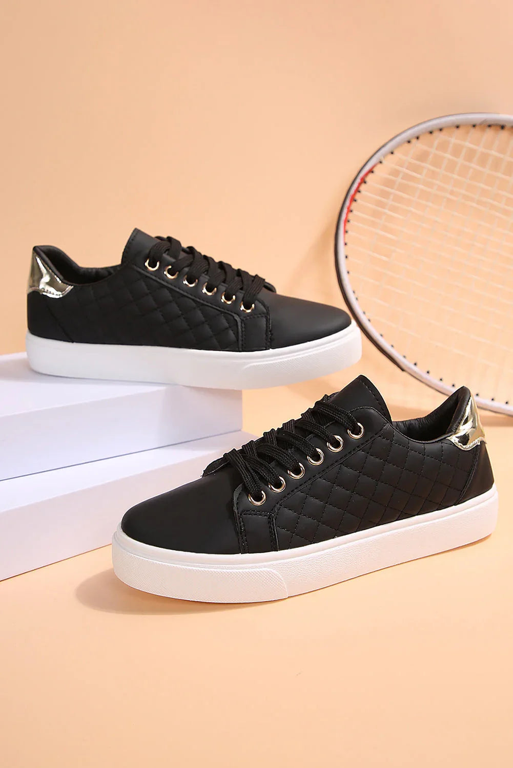 Black quilted women’s sneakers with white soles and metallic gold heel accents on a beige background