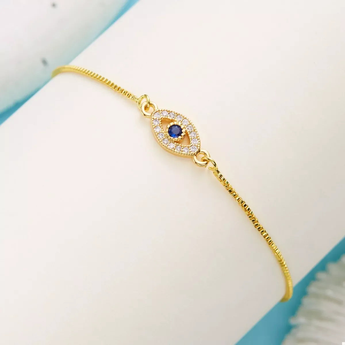 Gold bracelet with blue gemstone and crystal evil eye charm on neutral background
