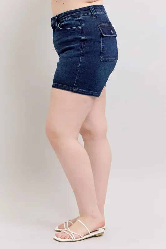 Woman wearing high-waisted dark denim shorts and white sandals, side view, studio background