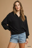 Woman wearing a relaxed black pullover top and denim shorts against a beige background