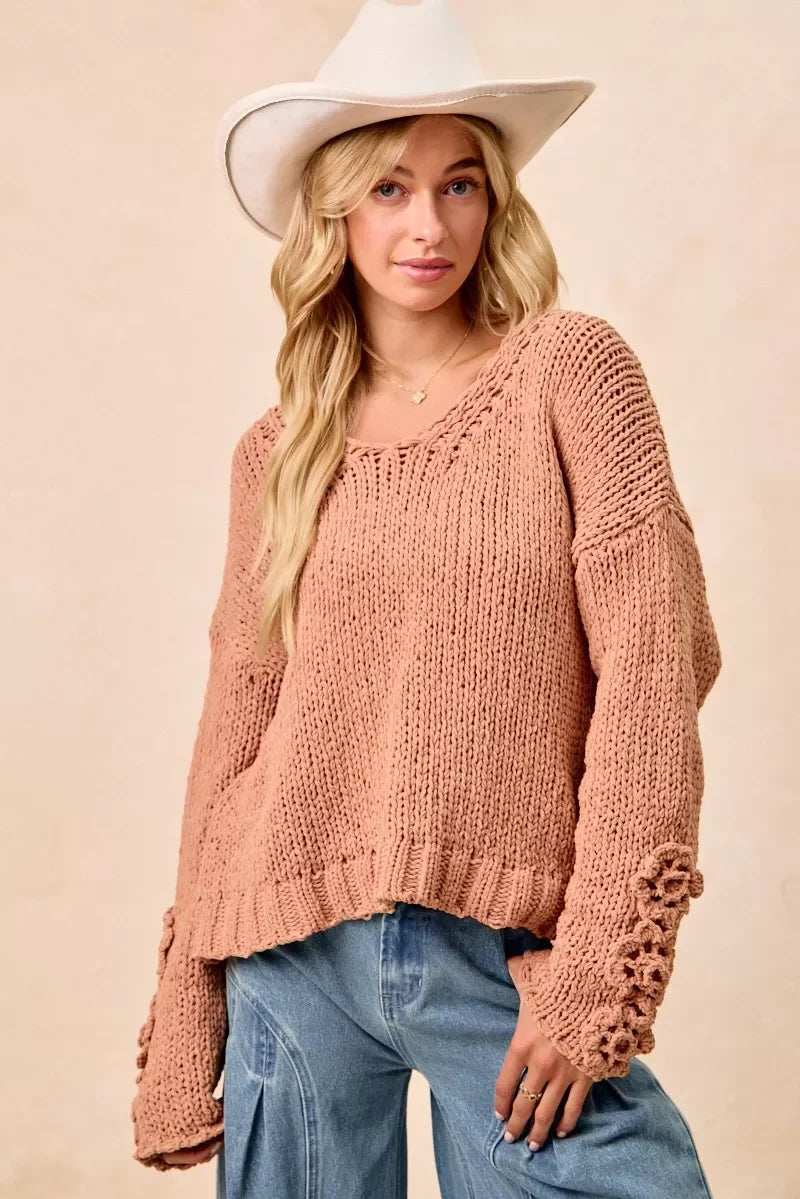 Woman in a beige chunky knit sweater with floral sleeve detail, cowboy hat, and relaxed jeans