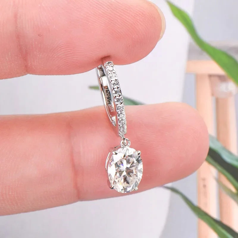 Hand holding a silver hoop earring with small pavé stones and a large round clear gemstone drop