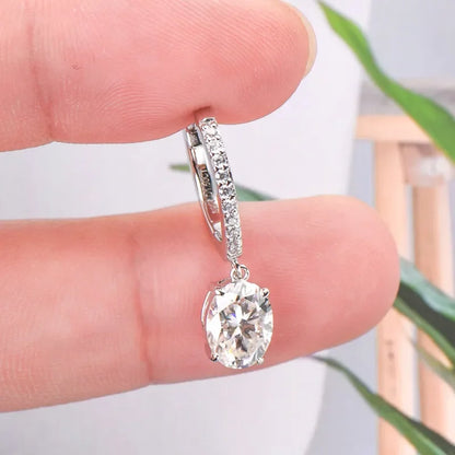 Hand holding a silver hoop earring with small pavé stones and a large round clear gemstone drop