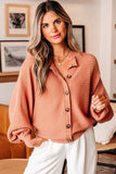 Woman wearing a relaxed, ribbed mauve button-up sweater with white pants in a modern living room.