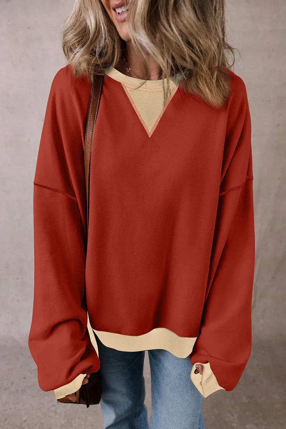 Woman wearing oversized red pullover sweater with beige trim and light blue jeans