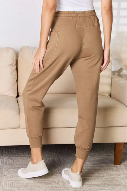 Woman wearing tan jogger pants with pockets, standing in a cozy living room setting.
