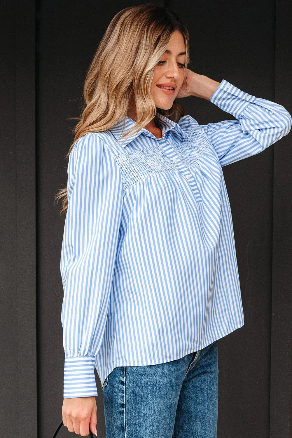Woman wearing a blue and white striped blouse with smocked detail and denim jeans