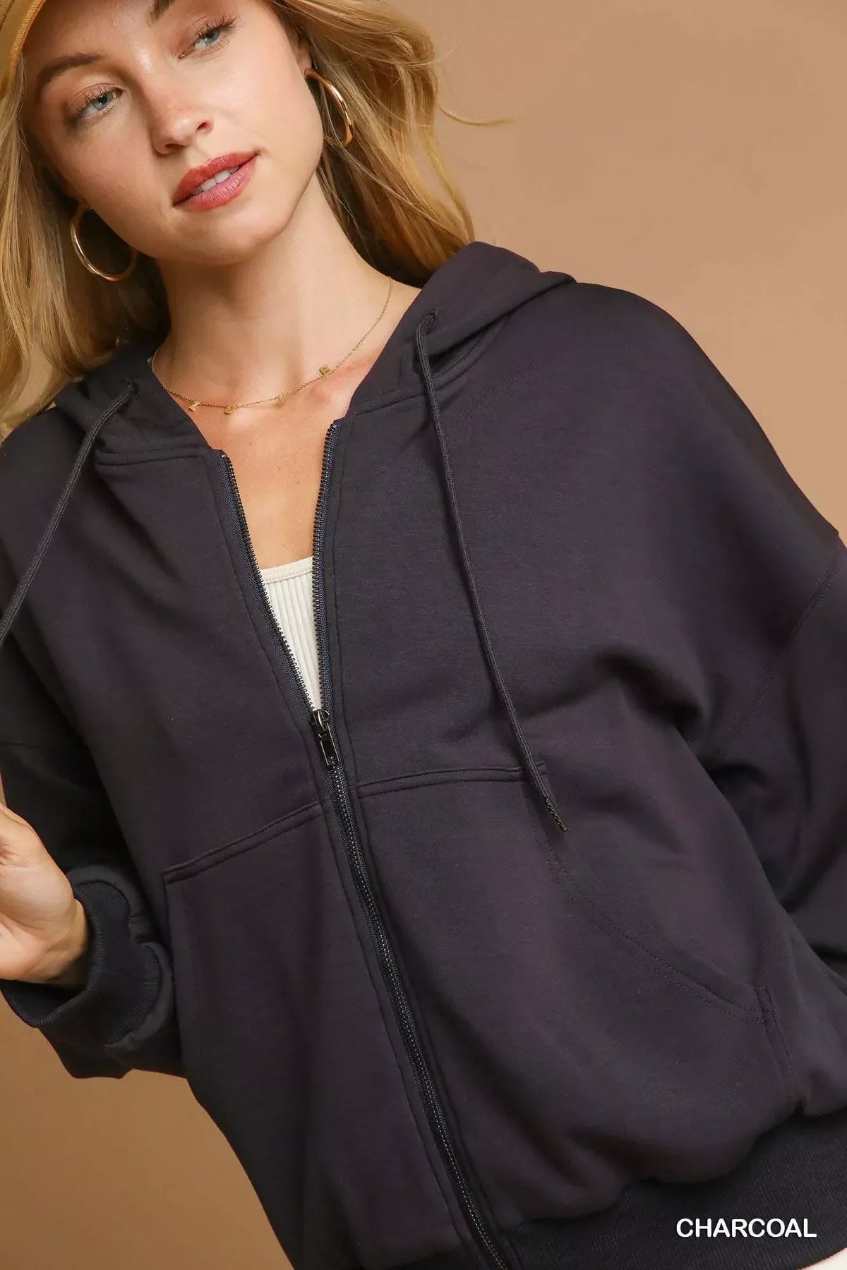 Woman wearing charcoal zip-up hoodie with front pockets and a hood, casual neutral background