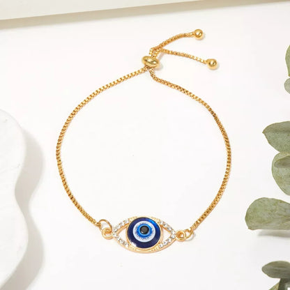 Gold adjustable bracelet with blue evil eye charm and clear crystal accents on white background