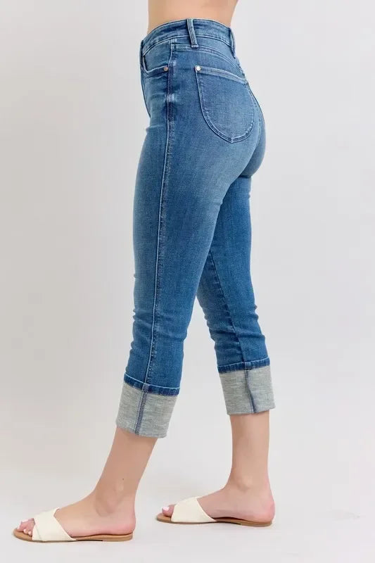 High-waisted cropped blue jeans with cuffed hems, styled with white slide sandals.
