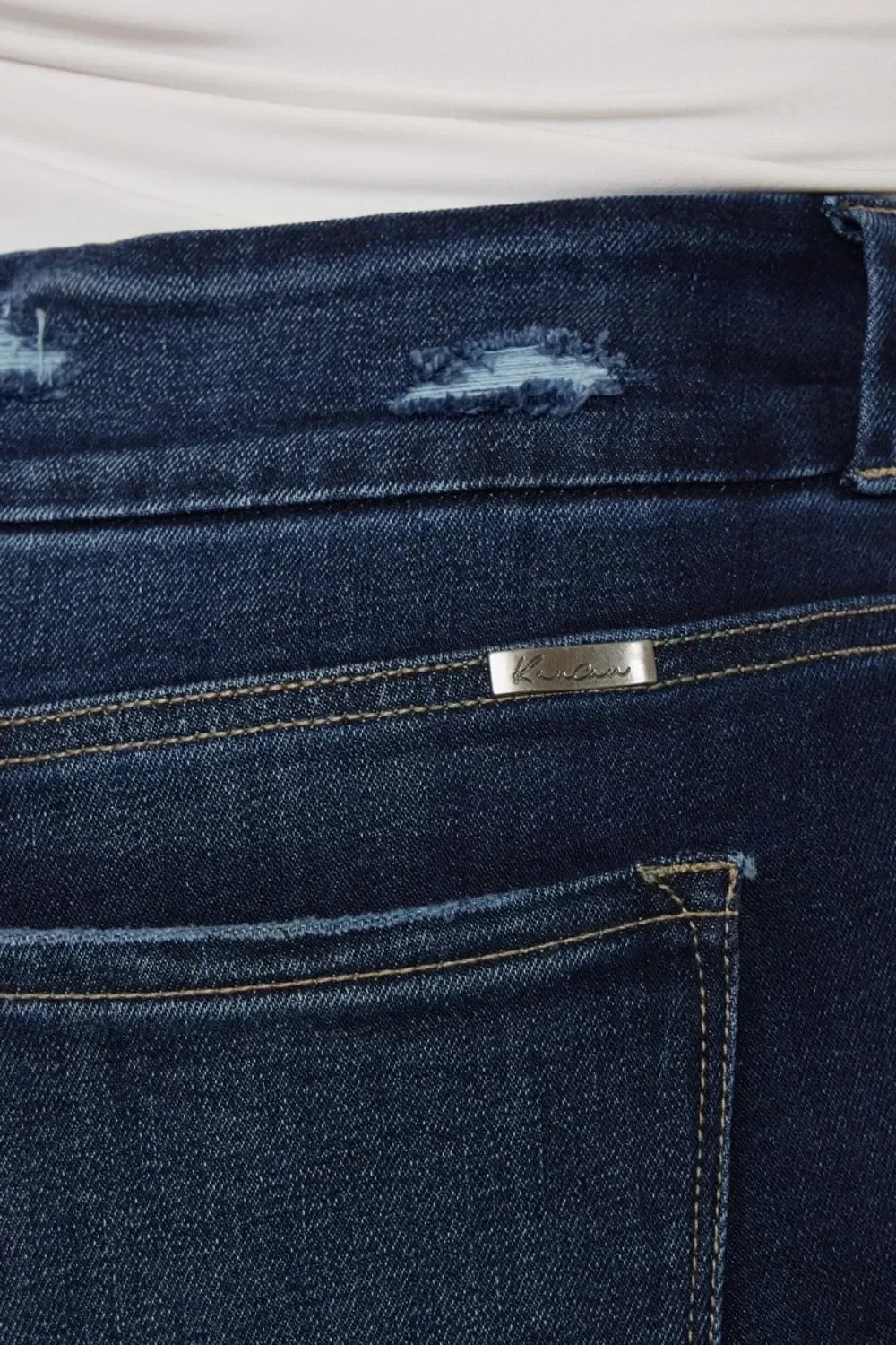 Close-up of dark blue denim jeans with distressing and a metal tag detail.
