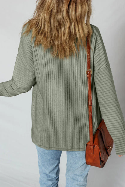 Woman in a sage green ribbed knit sweater, blue jeans, and brown leather shoulder bag