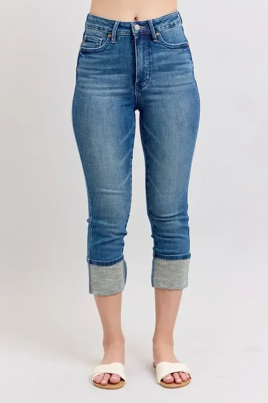 High-waisted blue cropped jeans with wide cuffed hems, styled with white sandals.