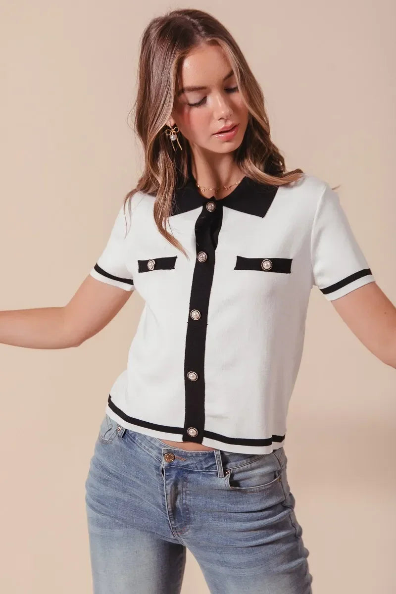 Woman wearing a short sleeve white knit top with black trim, pearl buttons, and blue jeans