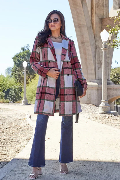 Woman wearing a pink plaid coat, white top, and flared jeans outdoors under bridge.