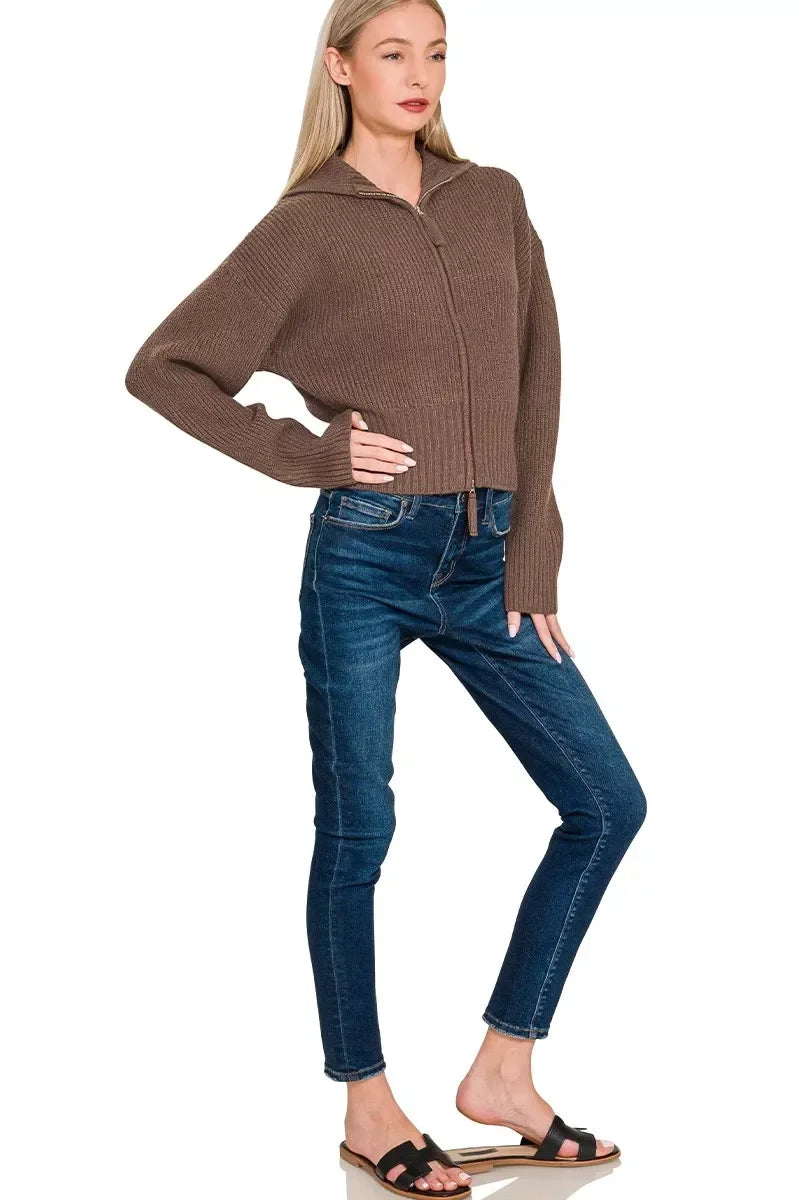 Woman wearing a brown ribbed zip-up sweater, blue skinny jeans, and black sandals