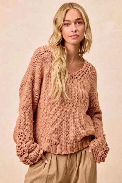 Woman in relaxed fit, blush pink knit sweater with floral crochet sleeves and wide-leg pants