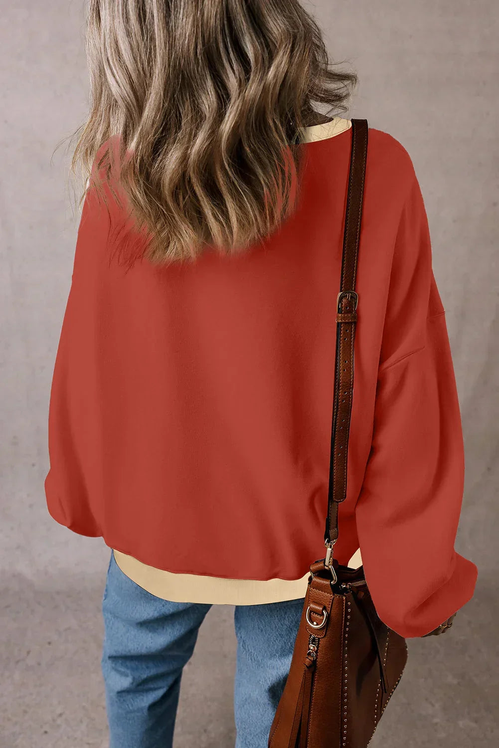 Woman in relaxed red sweater and blue jeans with brown leather shoulder bag, back view