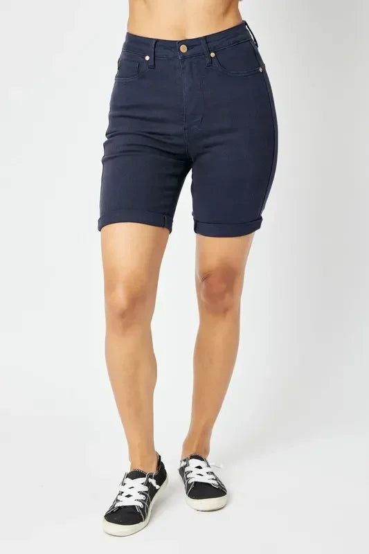 Woman wearing high-waisted dark denim Bermuda shorts with cuffed hems and black sneakers