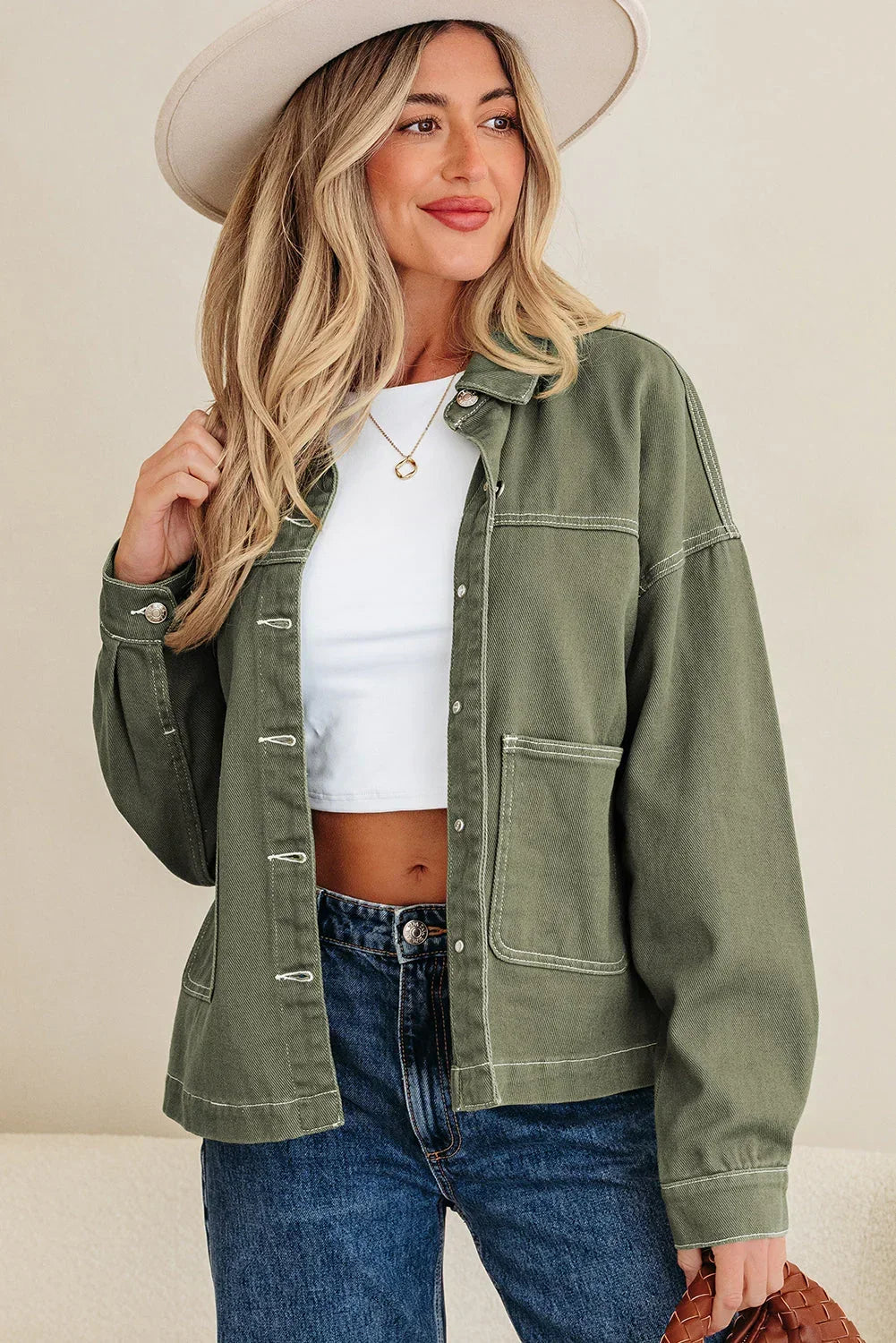 Woman in olive green jacket, white crop top, blue jeans, beige hat, modern casual style
