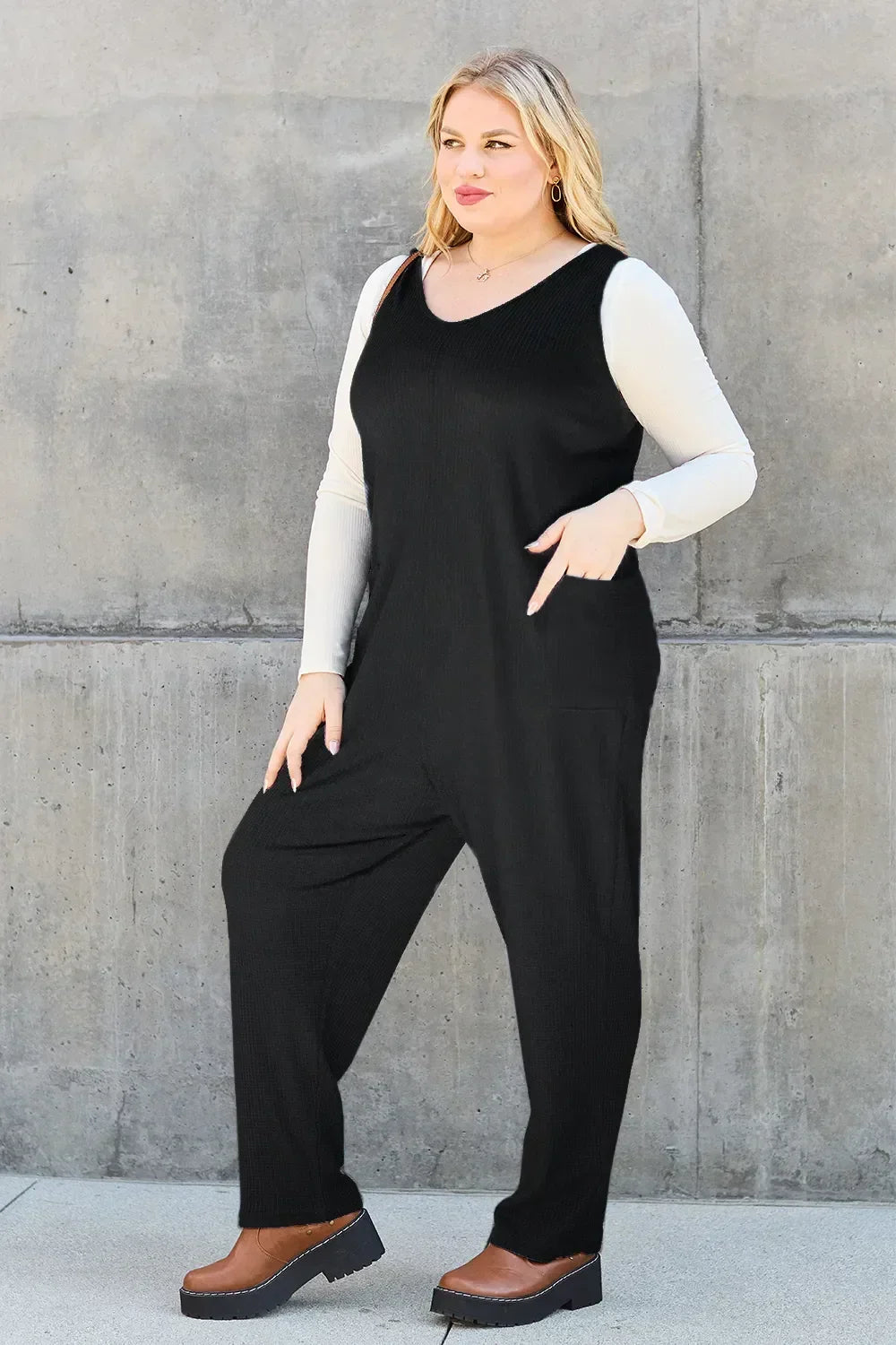 Woman in a black sleeveless jumpsuit over a cream long sleeve top and brown platform shoes