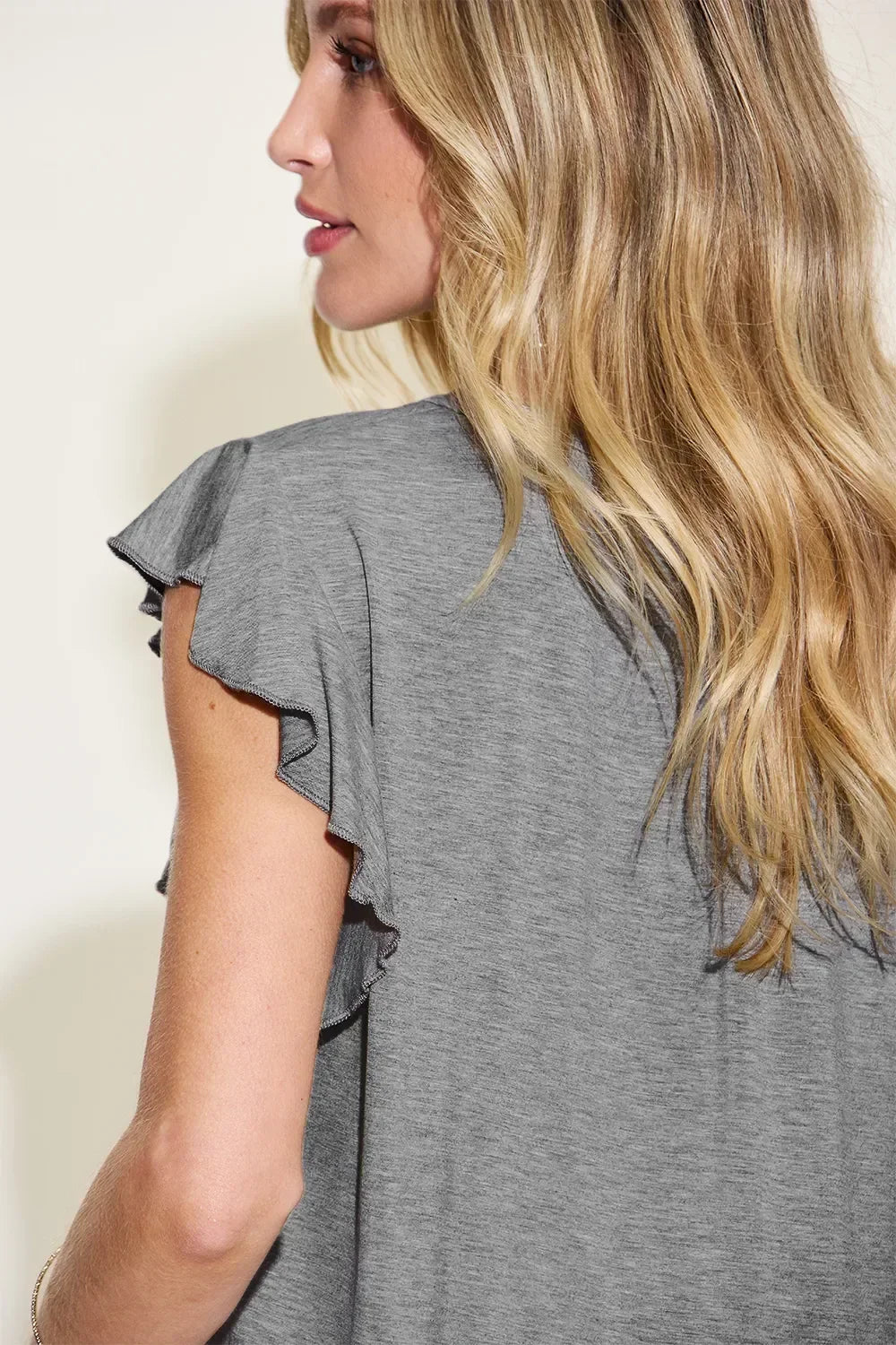 Woman in a heather grey ruffle sleeve top with relaxed fit, side and back view.