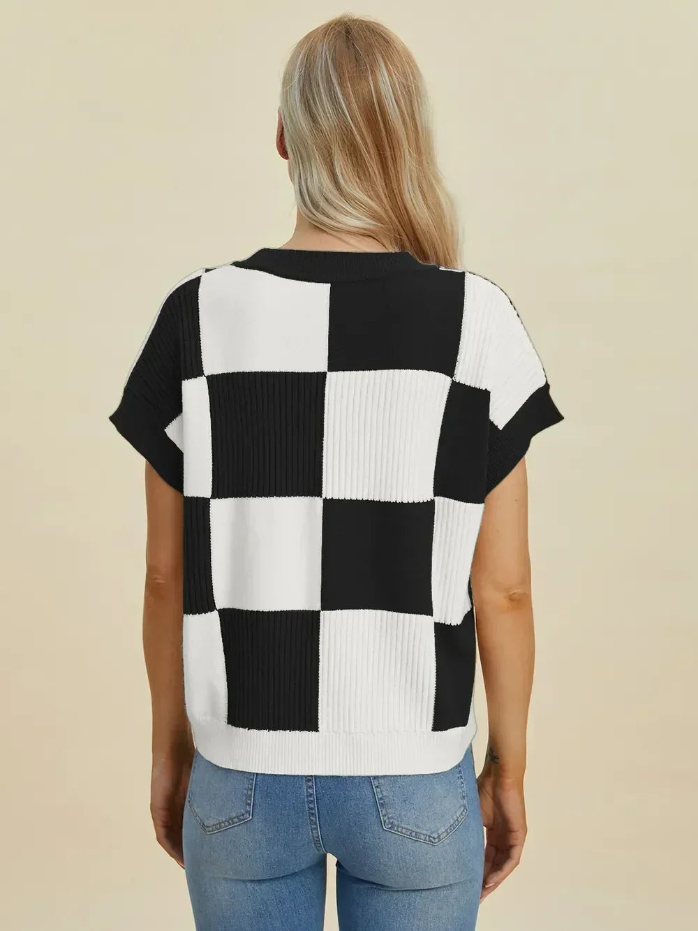 Woman wearing black and white checkered knit top with short sleeves and light blue jeans