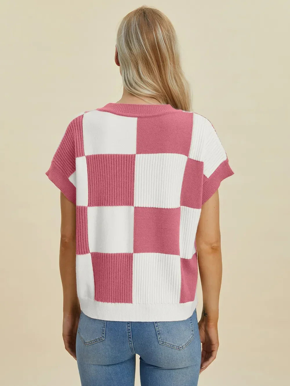 Woman wearing a pink and white checkered knit top with short sleeves and blue jeans, seen from behind.