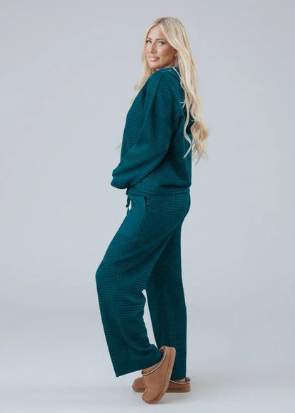 Woman wearing teal textured lounge set with wide leg pants and slippers, posing in studio.