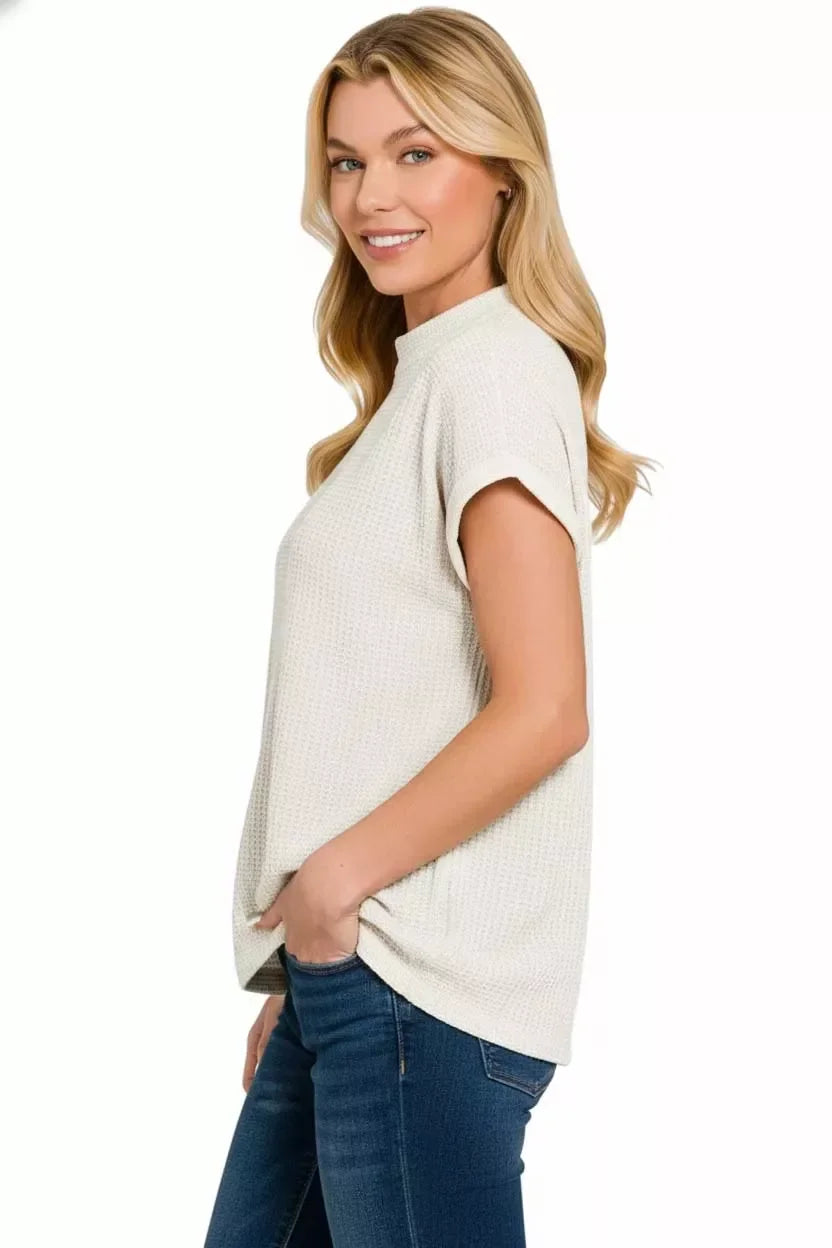 Woman in a textured ivory short sleeve top and blue jeans on white background
