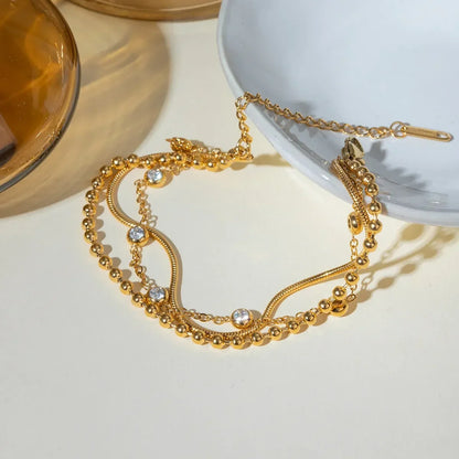 Gold layered bracelet with beads and clear crystals on a neutral background